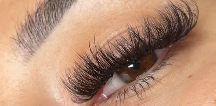 Side view of a full, spiky wispy lash set beneath a groomed brow